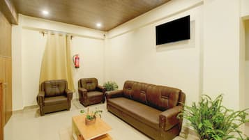 A living room with a brown leather sofa, two armchairs, a coffee table, and a flat-screen TV mounted on the wall.