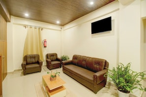 A living room with a brown leather sofa, two armchairs, a coffee table, and a flat-screen TV mounted on the wall.