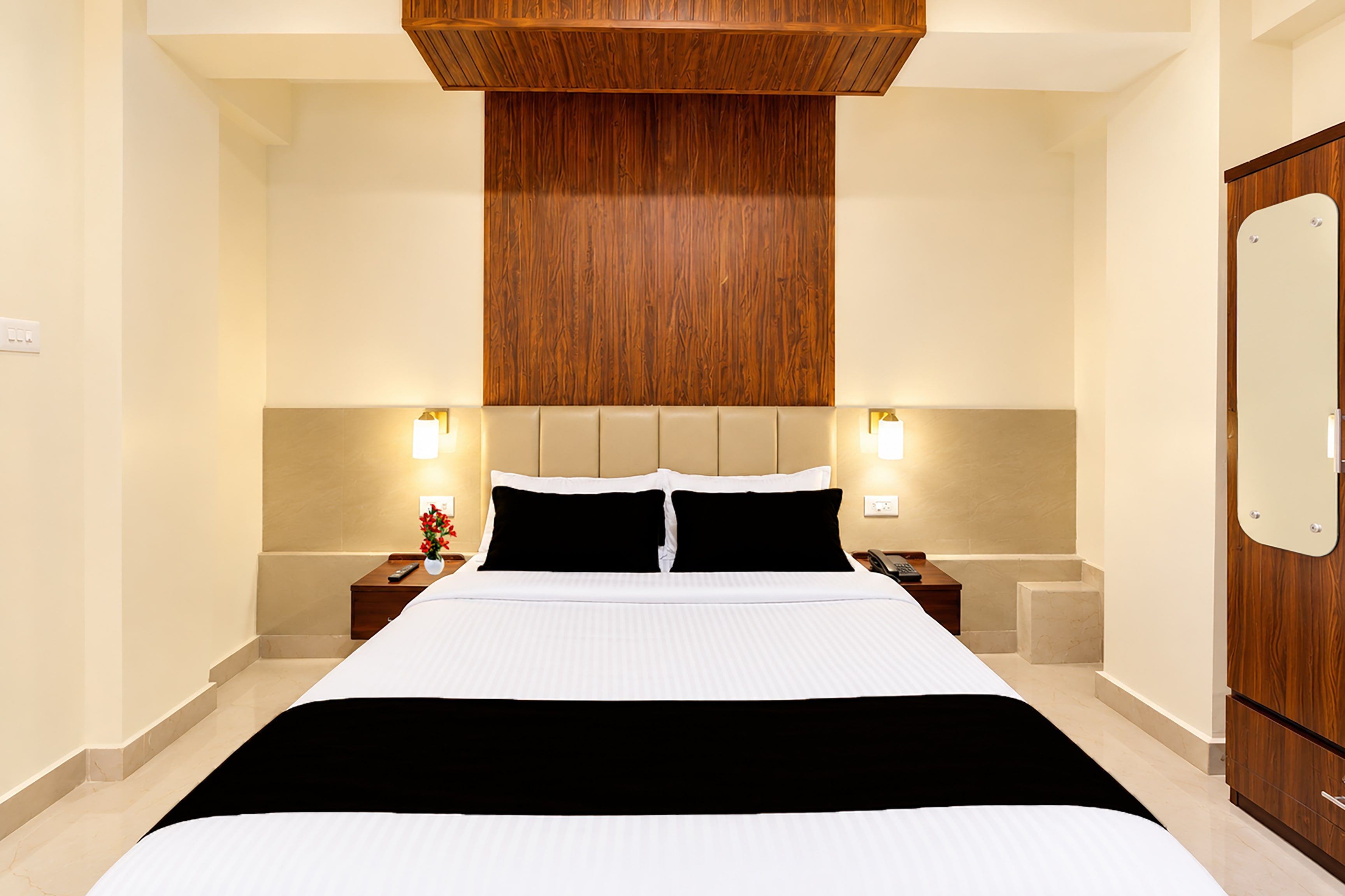 Een hotelkamer met een groot bed, een houten hoofdbord, nachtkastjes met lampen en een houten garderobe.
