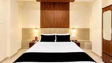 Een hotelkamer met een groot bed, een houten hoofdbord, nachtkastjes met lampen en een houten garderobe.