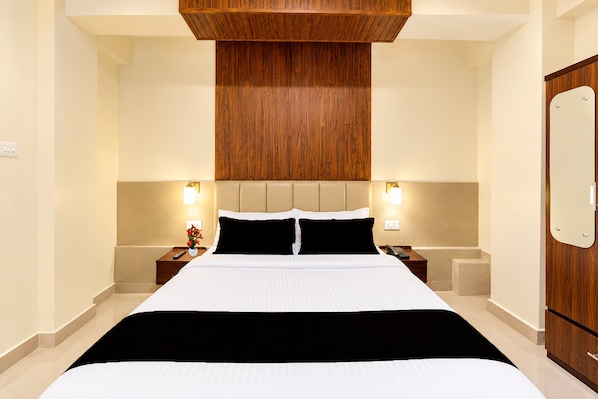 A hotel room with a large bed, wooden headboard, bedside tables with lamps, and a wooden wardrobe.
