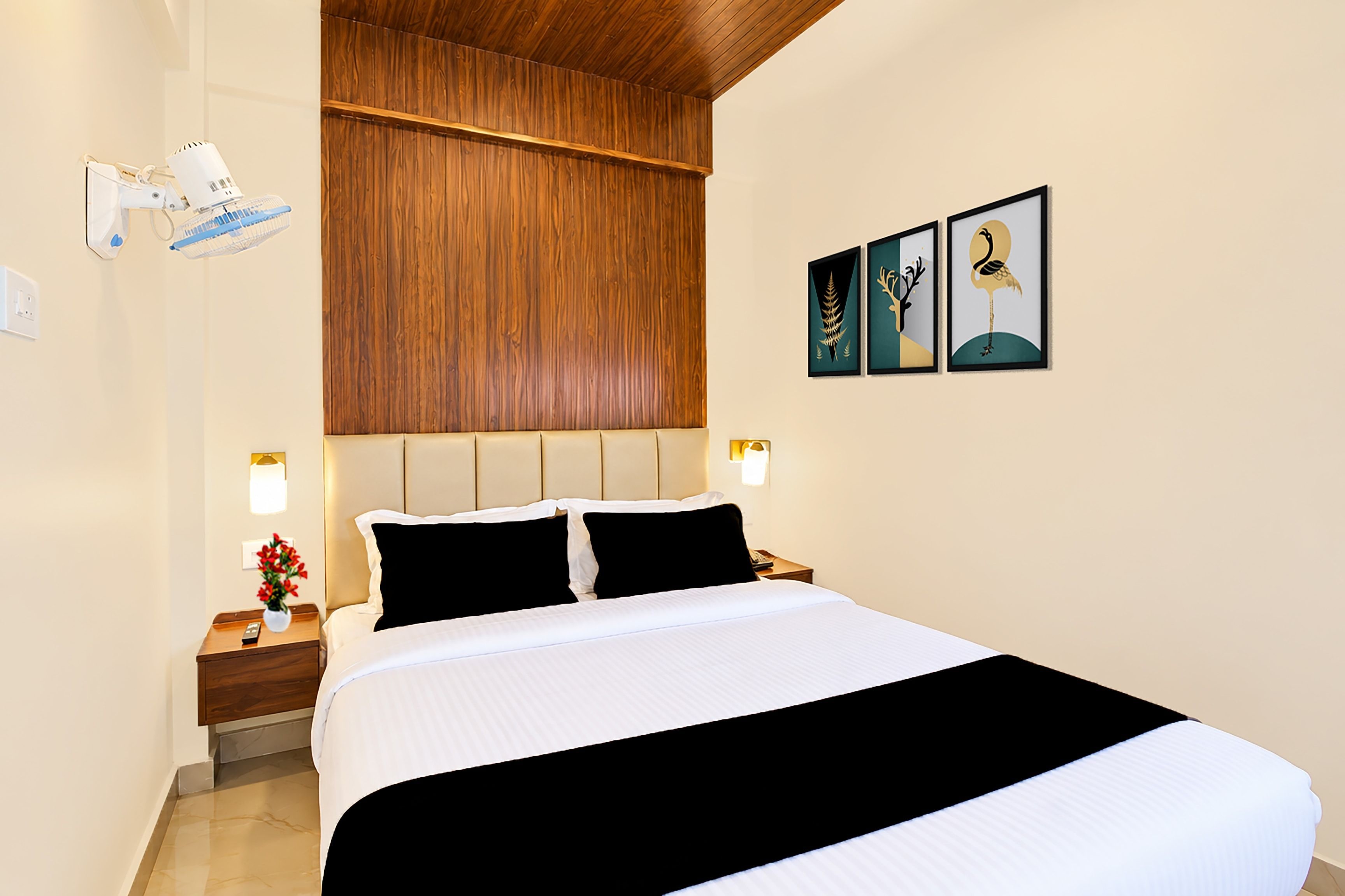 Una habitación de hotel con cama, mesitas de noche, cabecero de madera, un cuadro en la pared y un ventilador de techo.