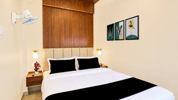 Una habitación de hotel con cama, mesitas de noche, cabecero de madera, un cuadro en la pared y un ventilador de techo.