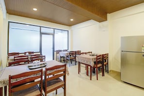 A dining area with wooden tables and chairs, a refrigerator, and a large window.