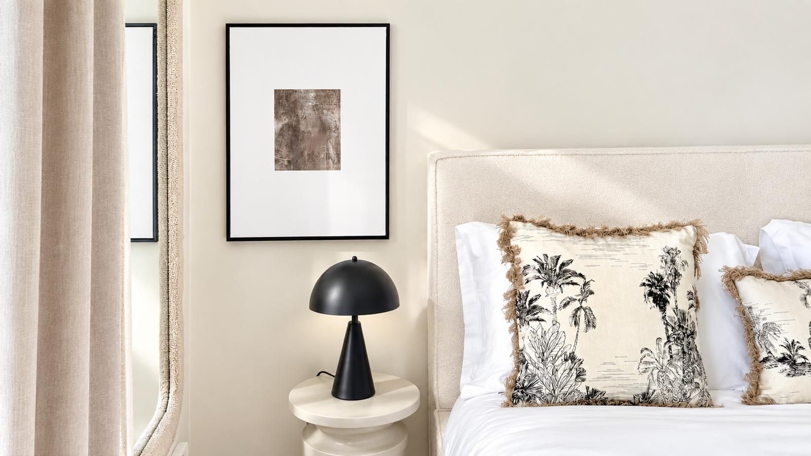 Ein Schlafzimmer mit einem Bett, Kissen, einem Nachttisch mit Lampe und einem gerahmten Bild an der Wand.
