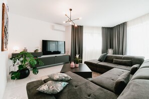 Ein modernes Wohnzimmer mit einem Flachbildfernseher, grauen Sofas, einem Couchtisch und einer Topfpflanze.