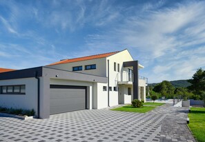Una casa moderna de dos pisos con garaje, balcón y entrada pavimentada.