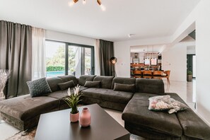 Un salon moderne avec un canapé d’angle, une table basse et un coin repas doté de chaises en bois.