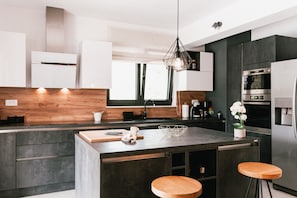 Eine moderne Küche mit einer zentralen Kochinsel, Holzhockern, einer Pendelleuchte und eingebauten Geräten.