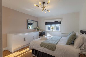 A bedroom with a bed, bedside table, dresser, mirror, window, and a chandelier.