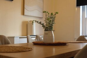 A dining table with a white vase containing a plant, surrounded by woven placemats.