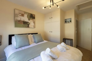 Ein Schlafzimmer mit Bett, Kissen, Decke, einem Gemälde, einem Kleiderschrank und einem kleinen Tisch.