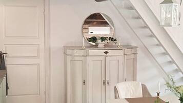 A room with a white door, a white cabinet with a mirror, a table with a vase, and a staircase.