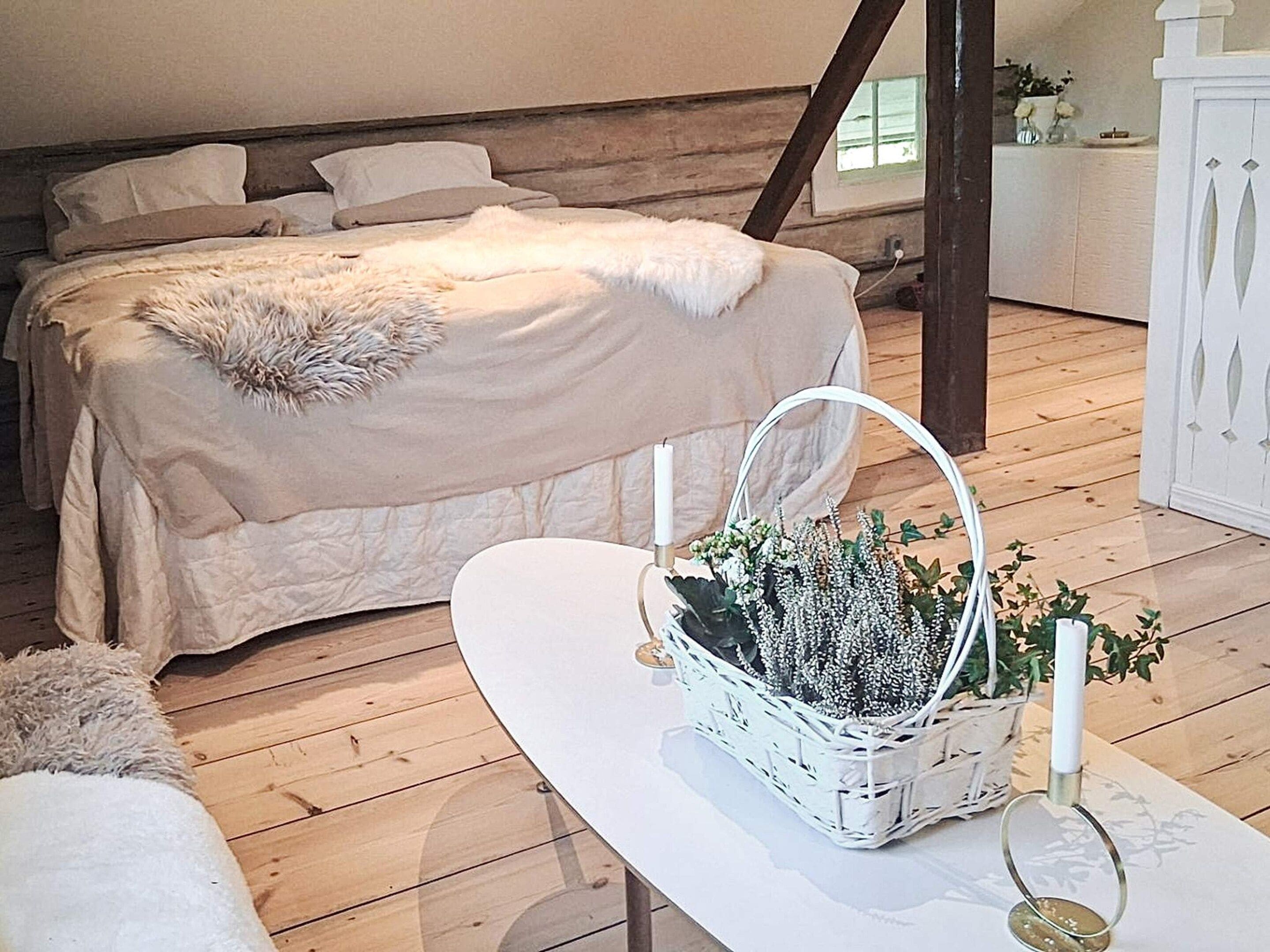 A bedroom with a bed, a white table with a basket, and a dresser.