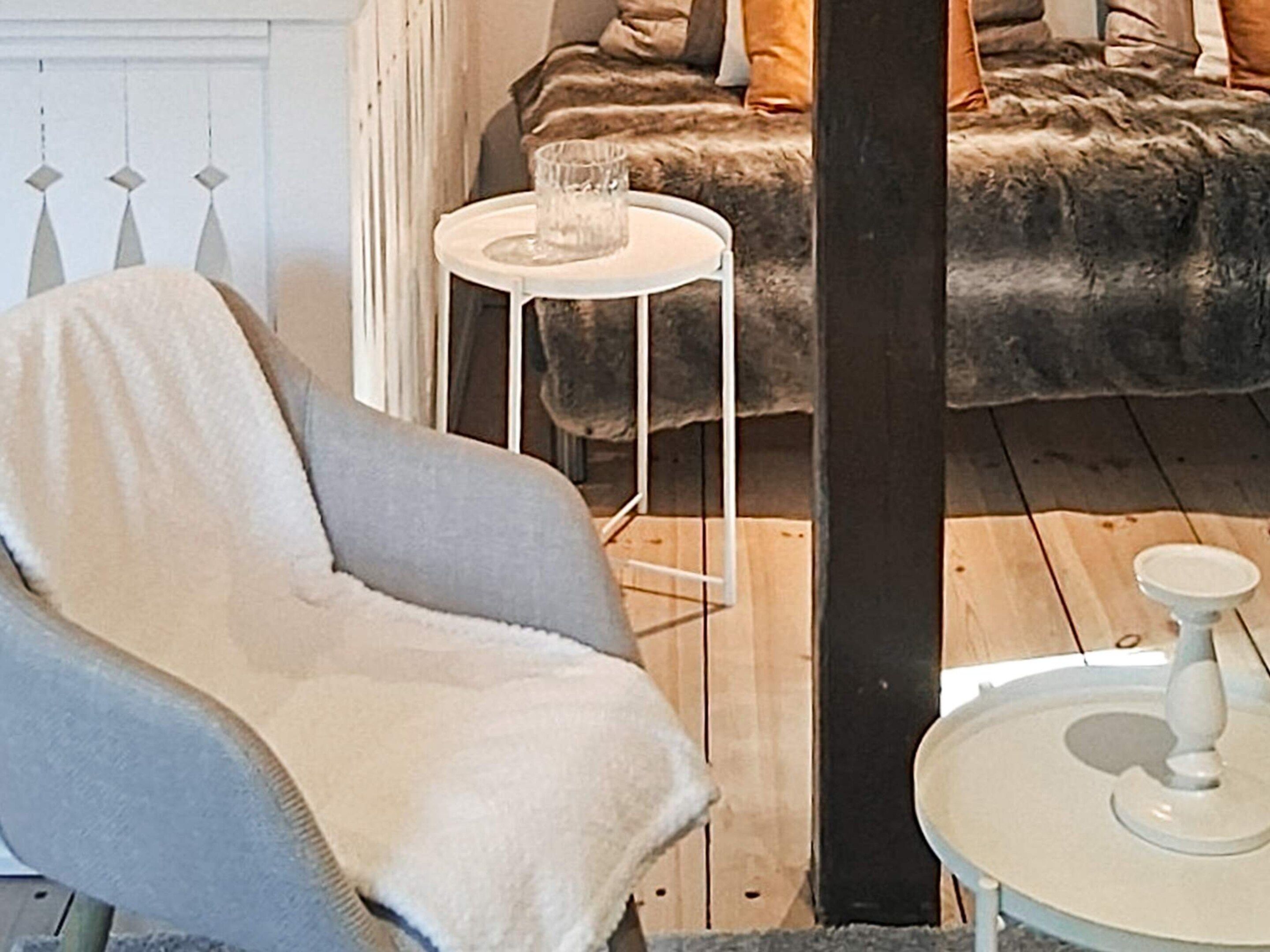 A cozy room with a plush sofa, a small white side table, and a chair with a blanket.