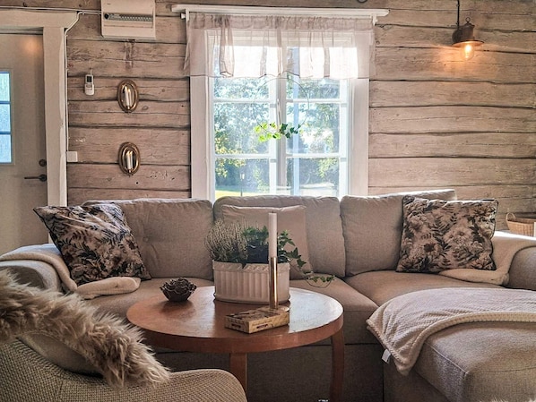 A cozy living room with a wooden wall, a sofa set, a round table, and a window with a view of greenery. - 7 Person Holiday Home in Osthammar (Osthammar)