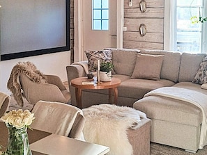 A living room with a sectional sofa, a round coffee table, and a white fur throw. - 7 Person Holiday Home in Osthammar (Osthammar)