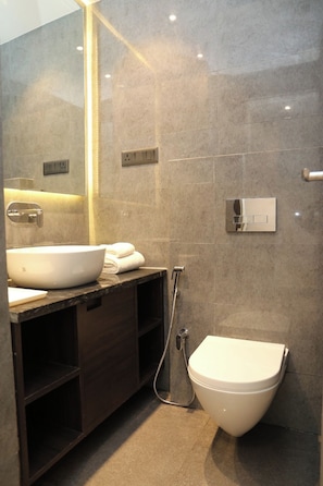 A modern bathroom with a large white sink, a dark wooden vanity, a white toilet, and a shower with a handheld showerhead.