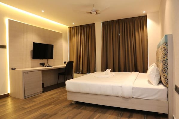 Una habitación de hotel con cama, escritorio, silla y televisión en la pared.