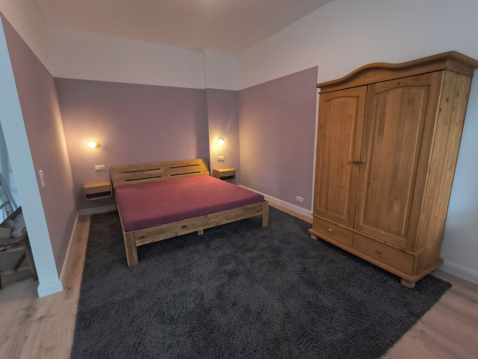 Une chambre avec un lit simple, une armoire en bois et deux lampes fixées au mur.