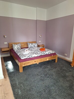 A bedroom with a wooden bed, a nightstand, and a wall socket.