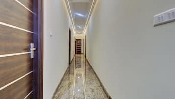 Un pasillo con una puerta de madera a la izquierda, una pared blanca a la derecha y suelo de mármol.