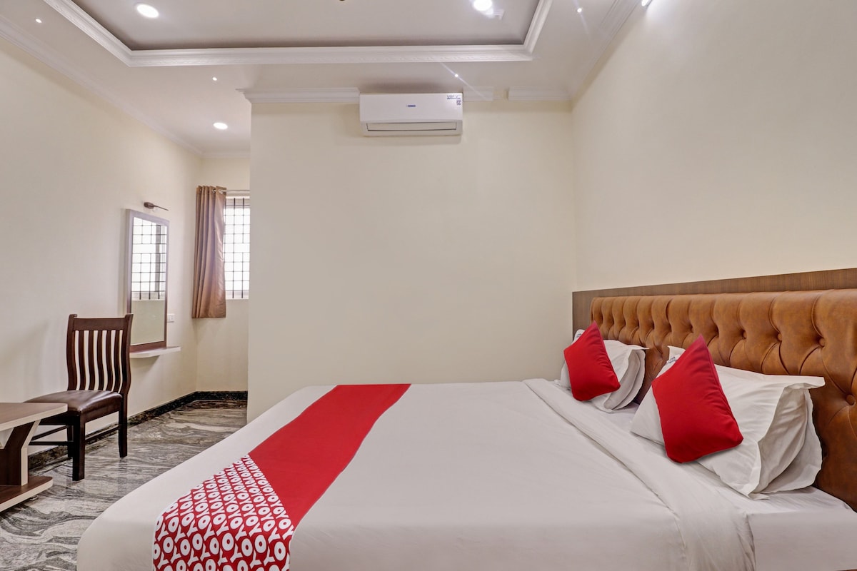 Een hotelkamer met een bed, een bureau en een stoel. Er is een airconditioningunit aan de muur.