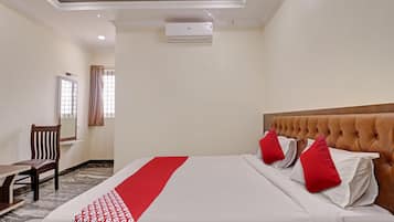 Een hotelkamer met een bed, een bureau en een stoel. Er is een airconditioningunit aan de muur.