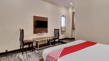 Een hotelkamer met een bed, een aan de muur bevestigde televisie, een bureau met stoel en een raam met gordijnen.