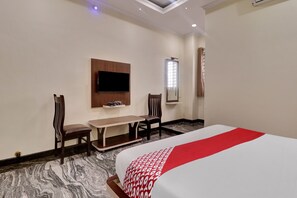 A hotel room with a bed, a TV mounted on the wall, a desk with a chair, and a window with curtains. - Collection O Ashraya Paradise (Bangalore)