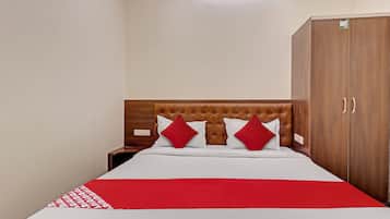 A hotel room with a large bed, a wooden wardrobe, and a nightstand.