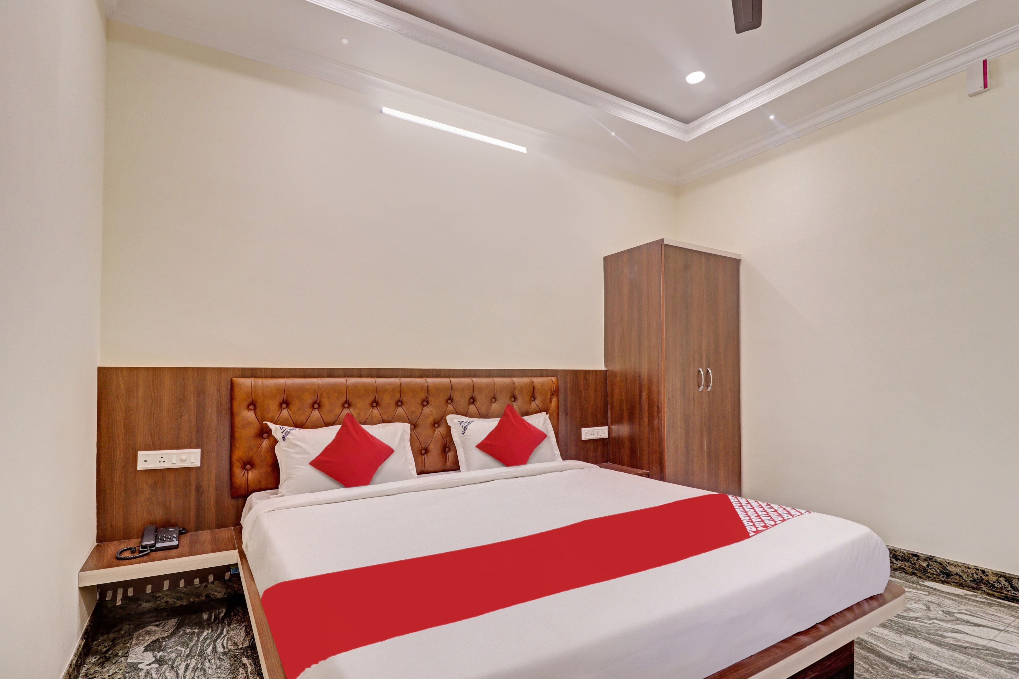 A hotel room with a large bed, a wooden headboard, a wardrobe, and a bedside table with a telephone.