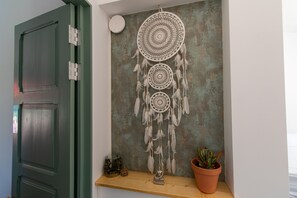 Une pièce avec une porte verte, un attrape-rêves accroché au mur, une petite statue de Bouddha et une plante en pot.