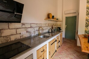 Une cuisine dotée d’une plaque de cuisson à induction noire, d’un évier en acier inoxydable, de meubles en bois et d’un dosseret carrelé.