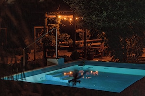 Ein Pool mit Stufen, umgeben von Grünpflanzen und einer Holzhütte mit Beleuchtung.