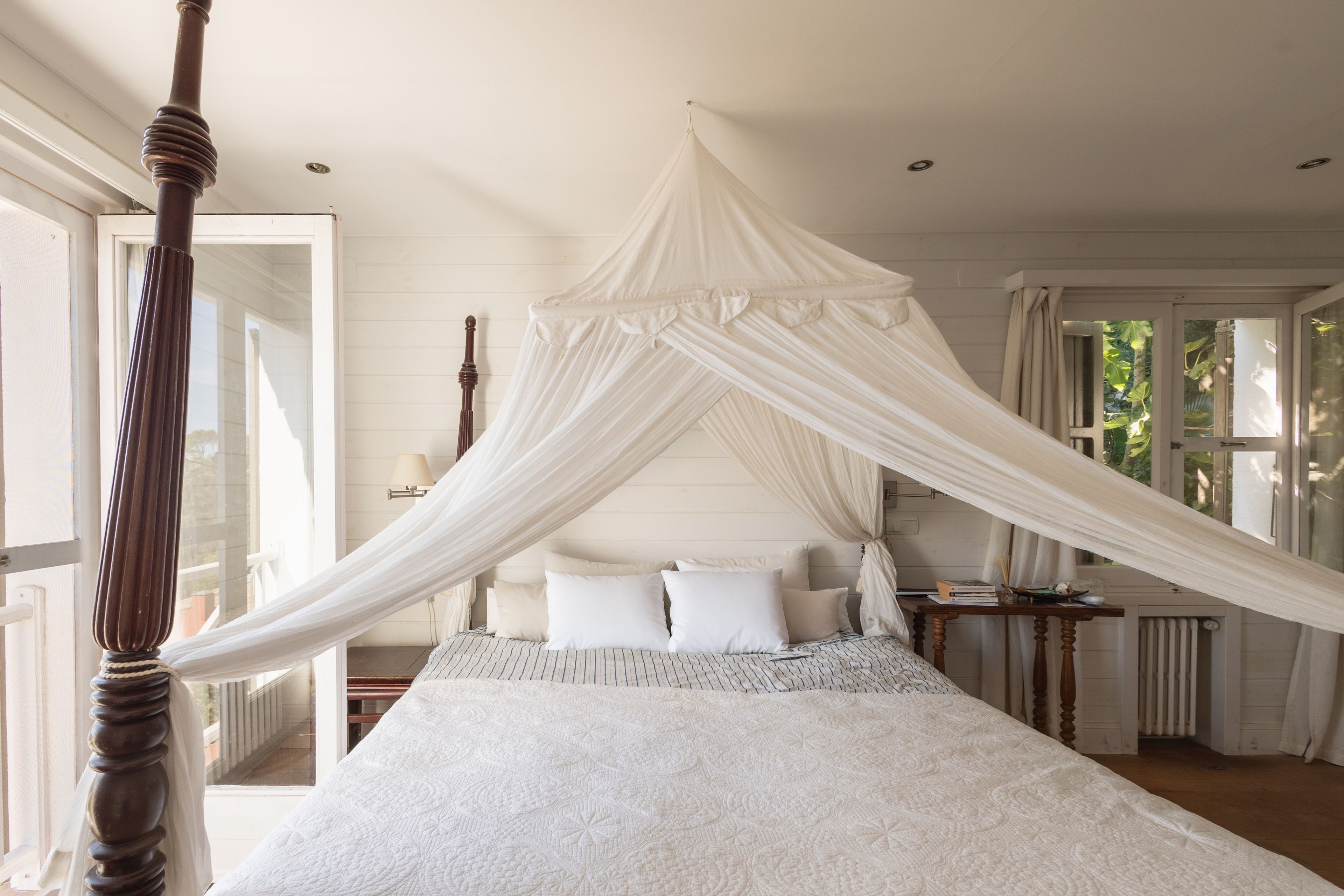 A bedroom with a canopy bed, wooden headboard, and a view of the outdoors.