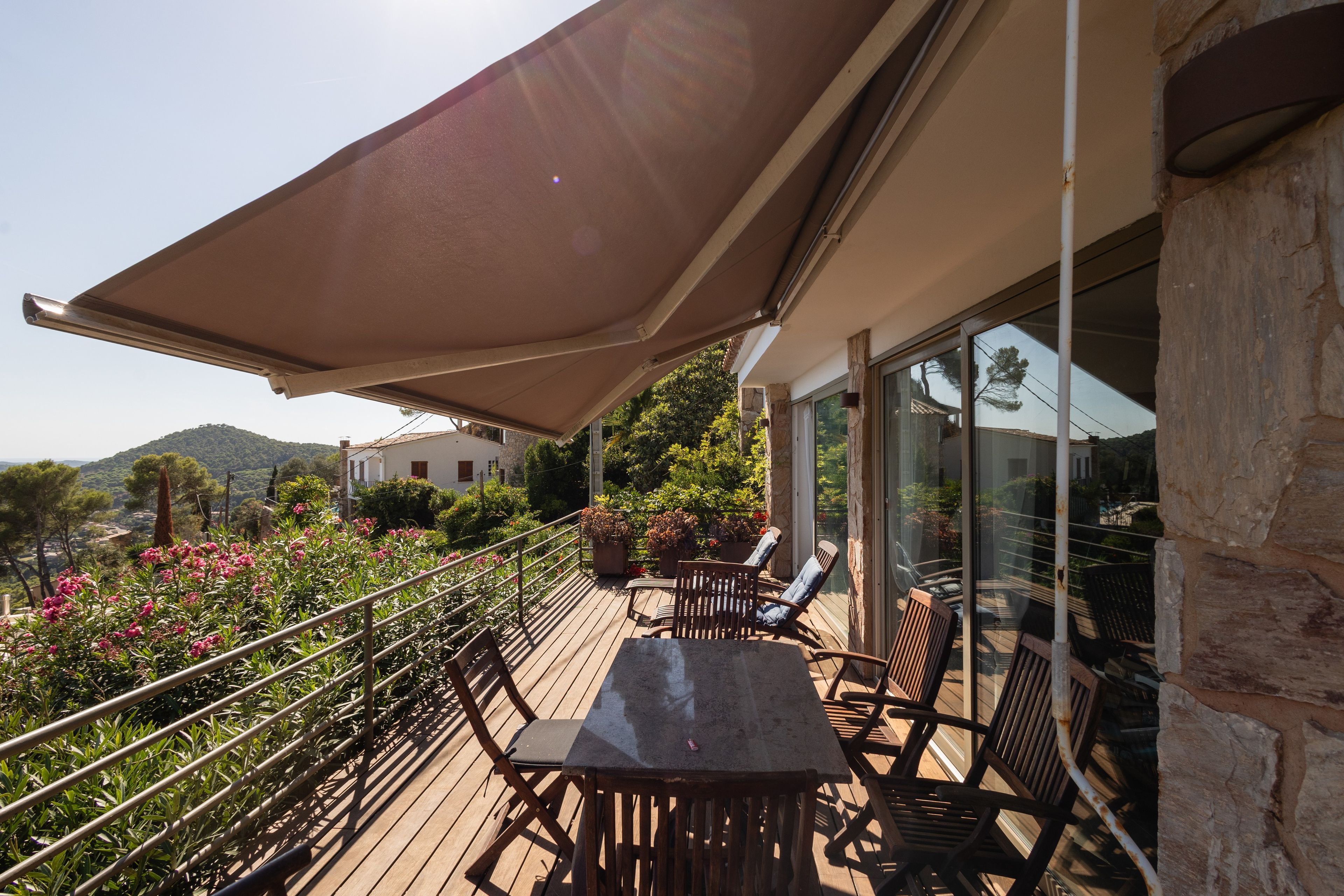 Une terrasse en bois, meublée pour l’extérieur, avec un grand parasol et une vue sur le paysage environnant.