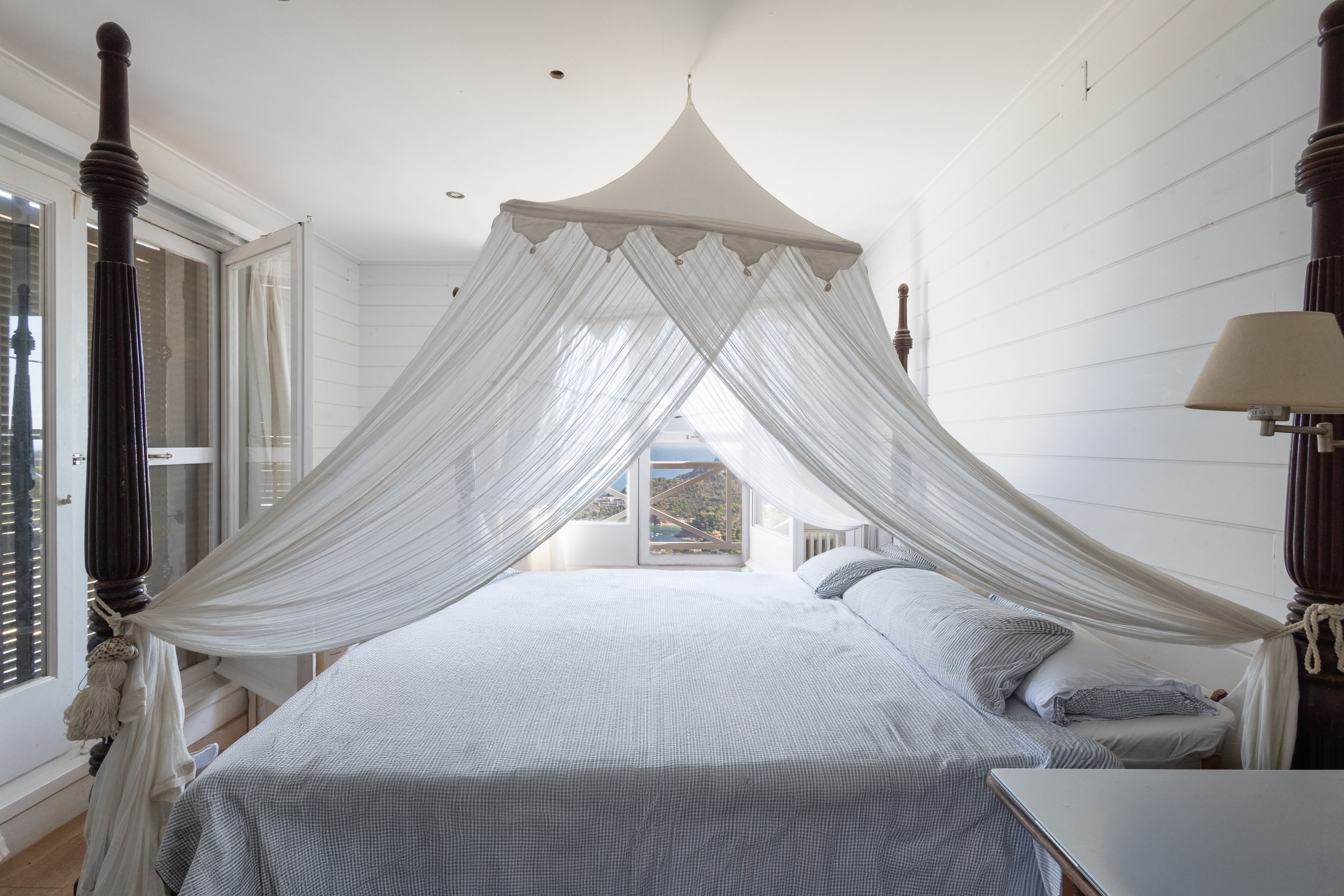 Une chambre à coucher avec un lit à baldaquin, un dais et une vue sur l’extérieur par une fenêtre.