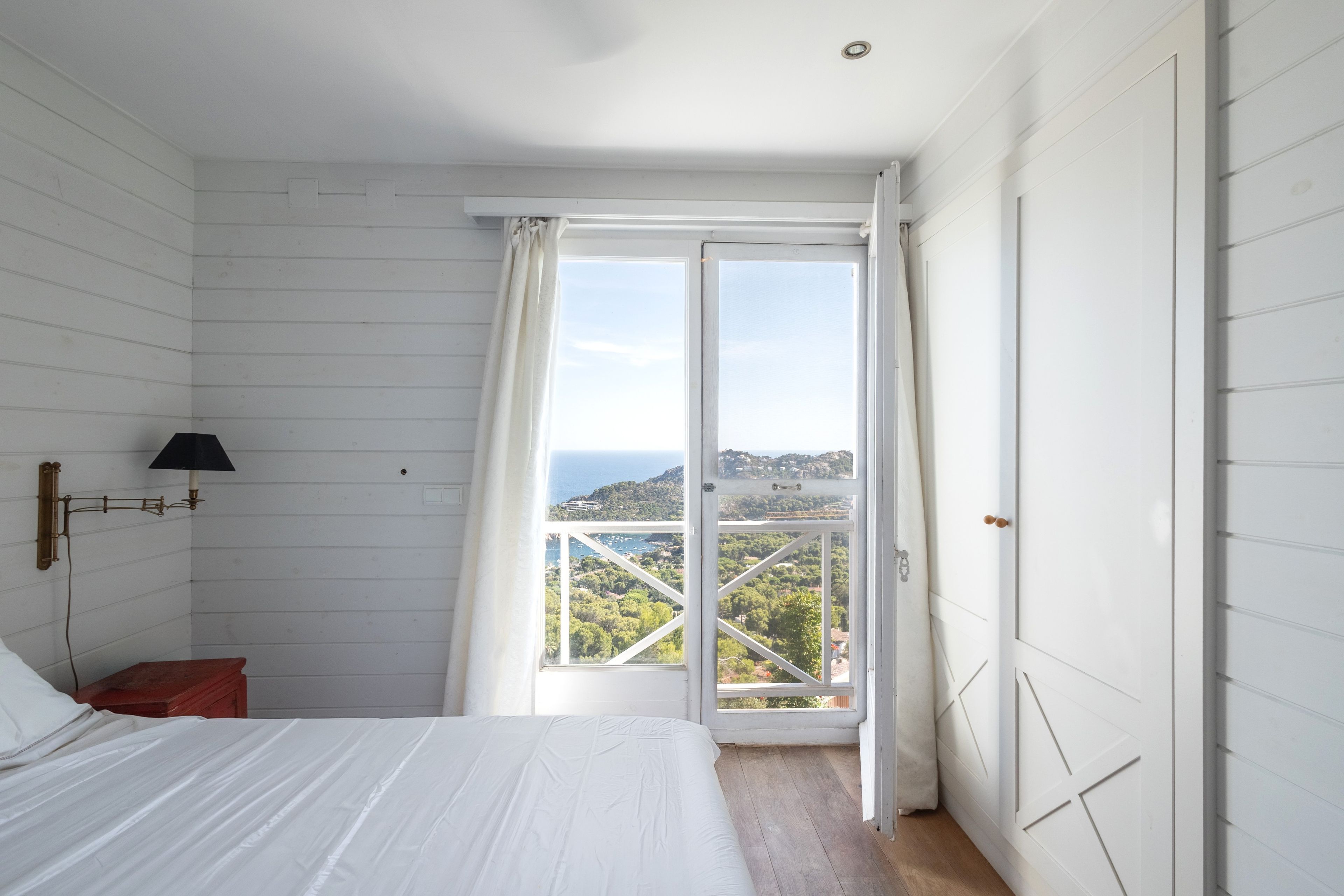 Un dormitorio con cama, mesita de noche, lámpara y ventana con vistas al paisaje.