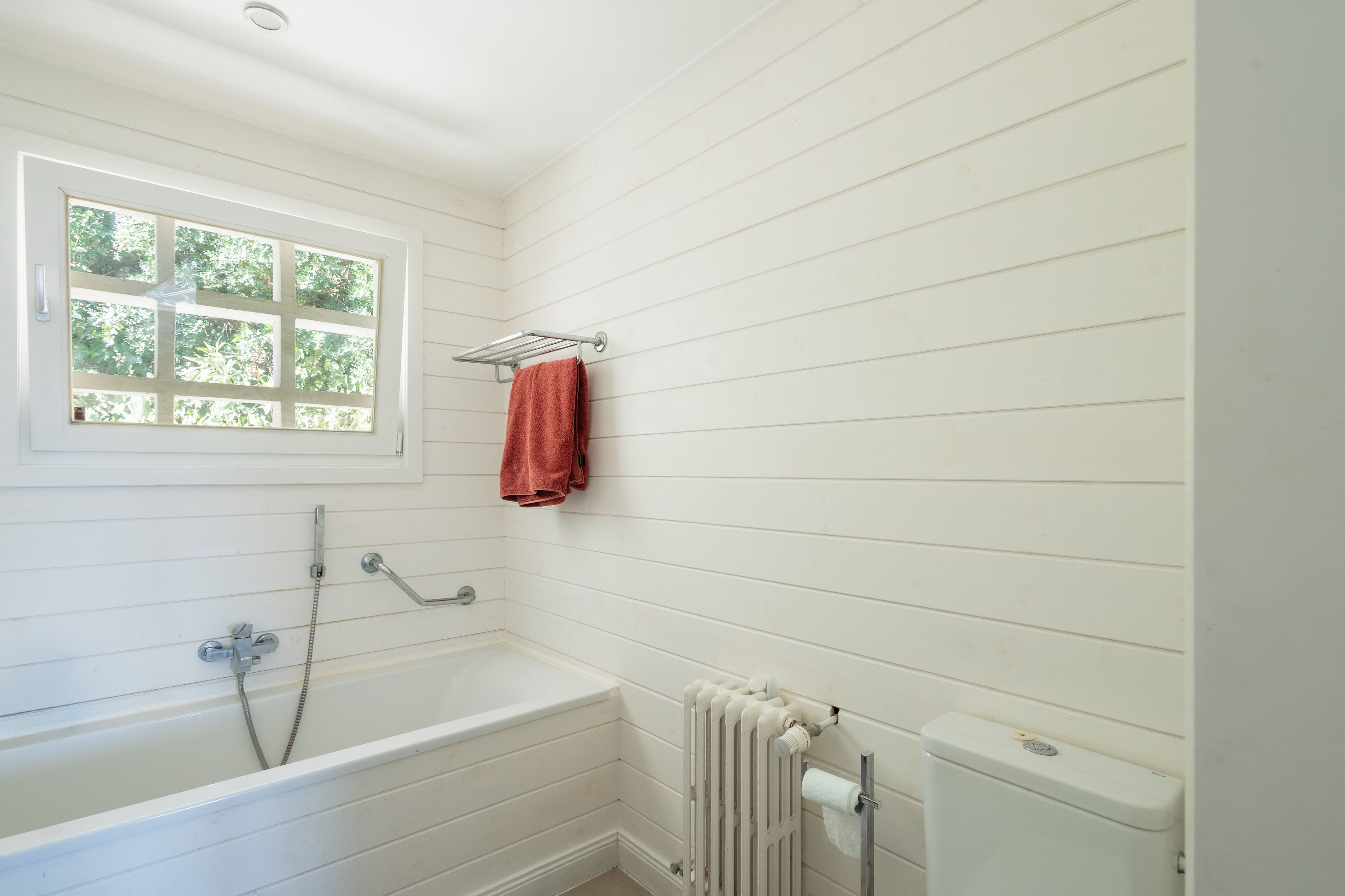 Een badkamer met een bad, een raam, een handdoekhouder en een toilet.
