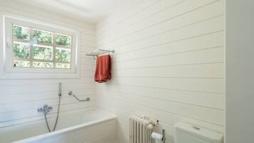 Een badkamer met een bad, een raam, een handdoekhouder en een toilet.