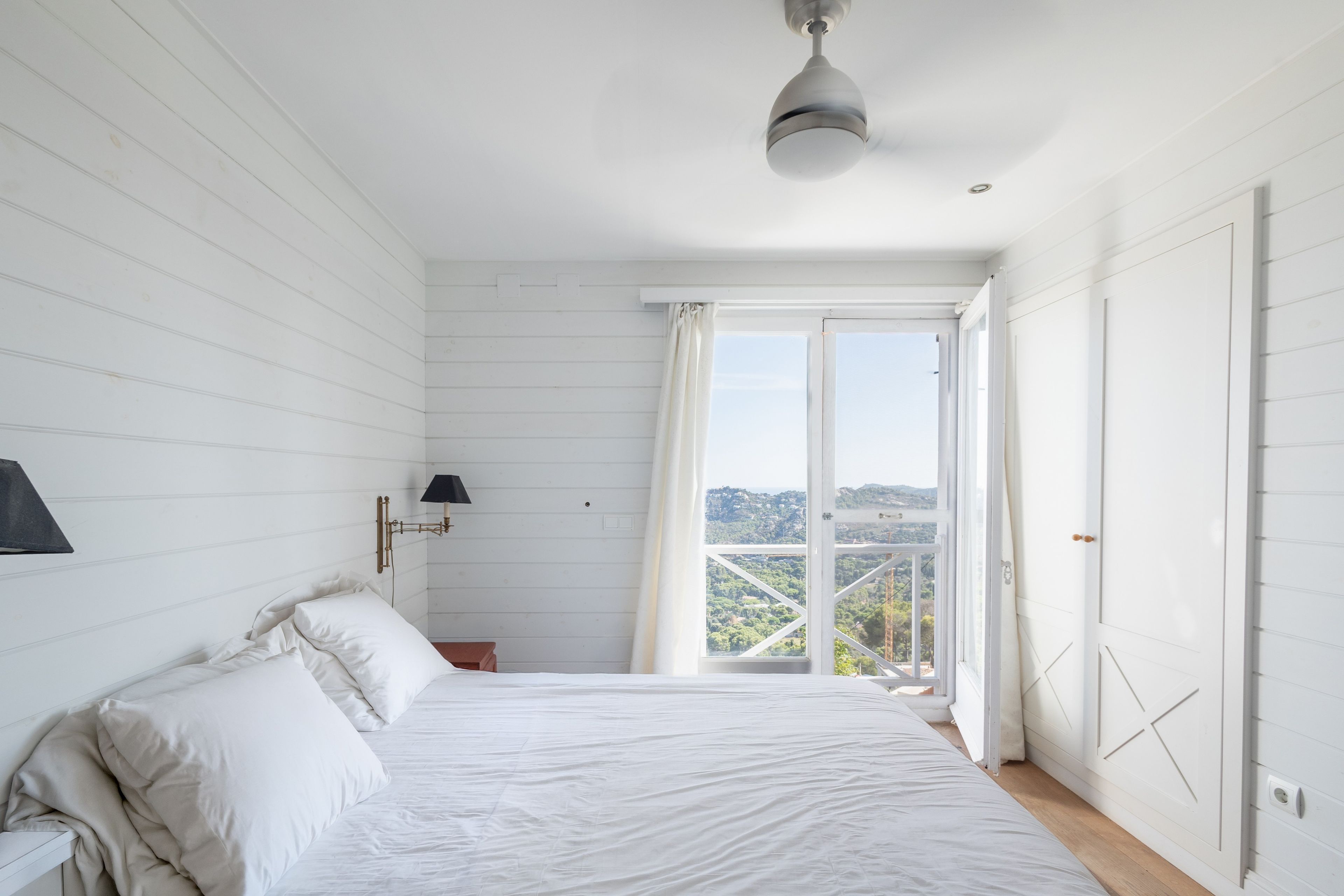 Une chambre à coucher comprenant un lit, une table de chevet, une lampe, une fenêtre avec des rideaux et une vue sur un paysage.