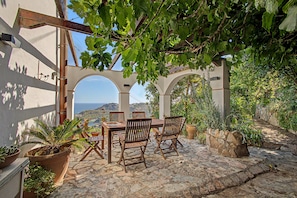An outdoor patio with a table and chairs, surrounded by greenery and overlooking a scenic view.