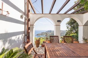 A wooden table and chairs under a pergola with a view of the sea and hills. - Holiday Home 'Ses Costes' with Sea View, Wi-Fi and Air Conditioning (Begur)