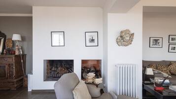 Een woonkamer met een open haard, een bank, een salontafel en een boekenkast.