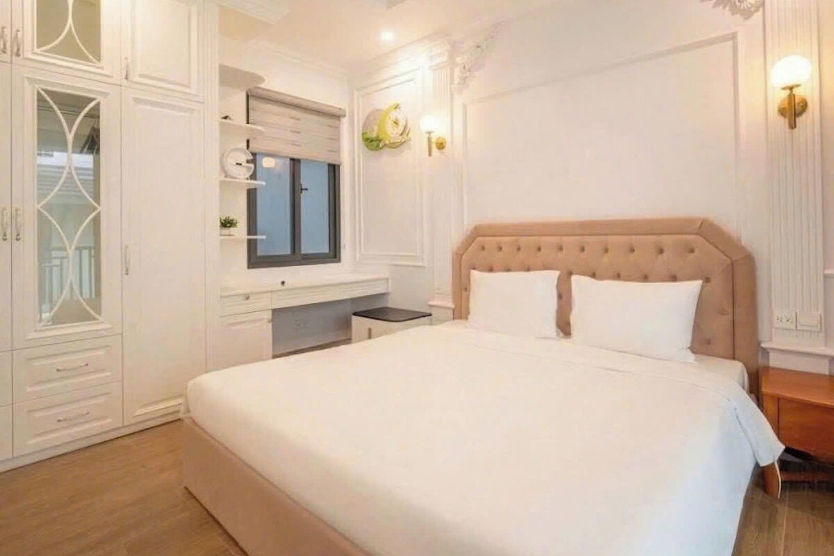 A bedroom with a large bed, a wardrobe, a desk, and a mirror.