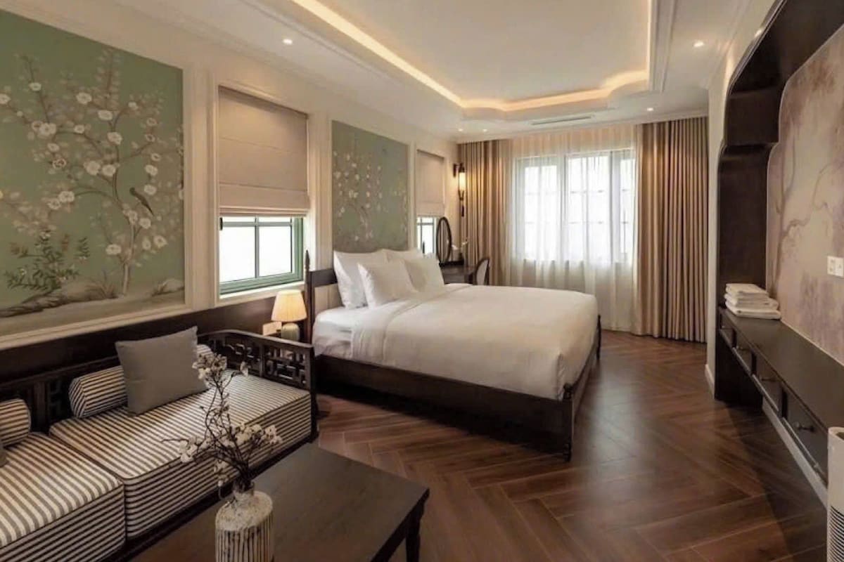 A hotel room with a large bed, a sofa, a nightstand, and a wall with floral wallpaper.