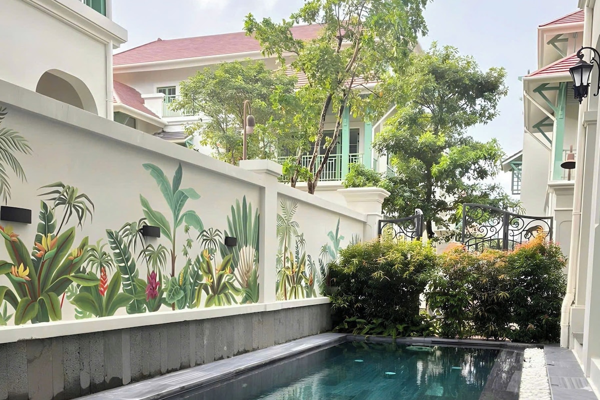 A swimming pool with a clear water surface, surrounded by a low wall with a tropical plant mural.