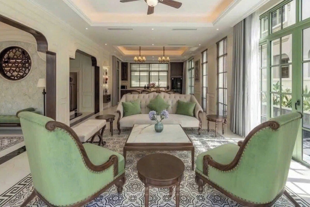 A spacious living area with a high ceiling, a ceiling fan, a sofa with green cushions, a coffee table, and patterned flooring.
