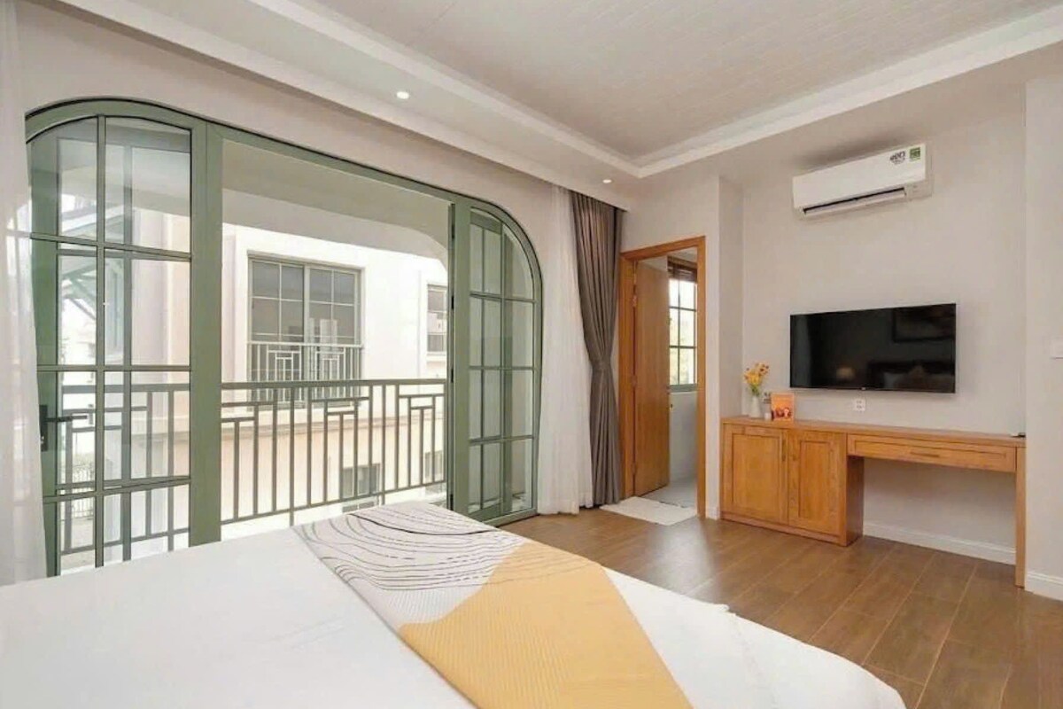A hotel room with a bed, a desk, a television, and a balcony with a view.